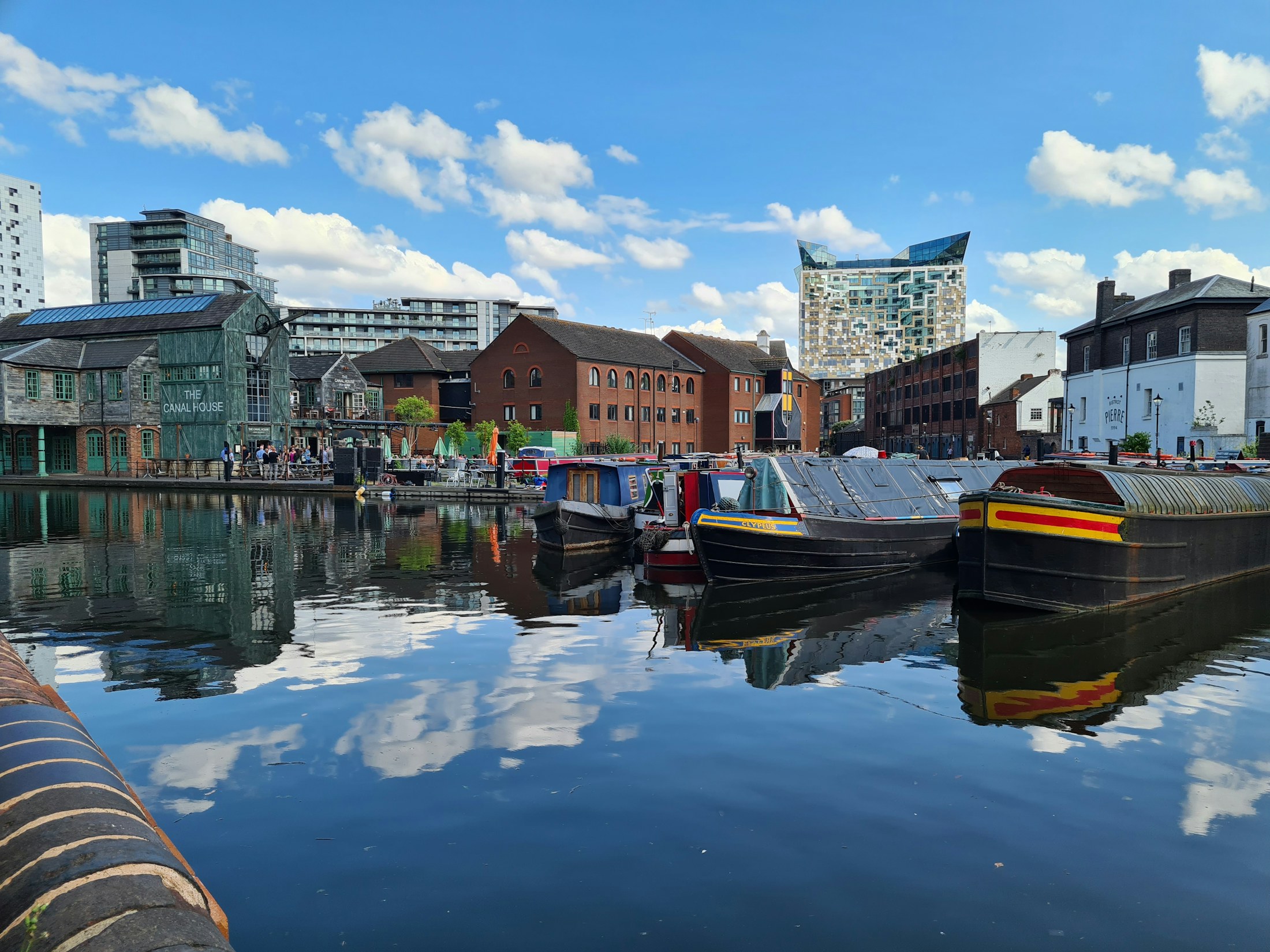 Barcos e fachadas coloridas nos canais de Birmingham em um dia de sol, com reflexos e céu azul