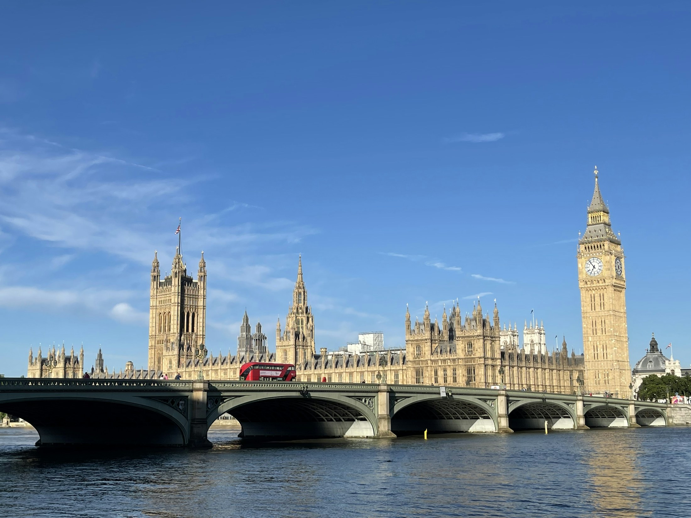 Sol da manhã sobre Westminster, Big Ben e a ponte, com céu azul e um ônibus vermelho